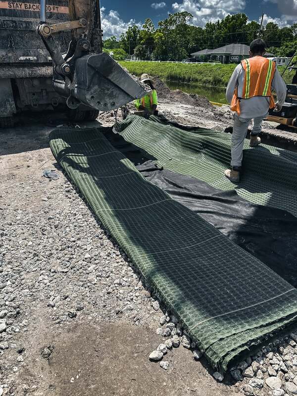 Workers rolling out Pyramat erosion control mat along a channel with aggregate ballast
