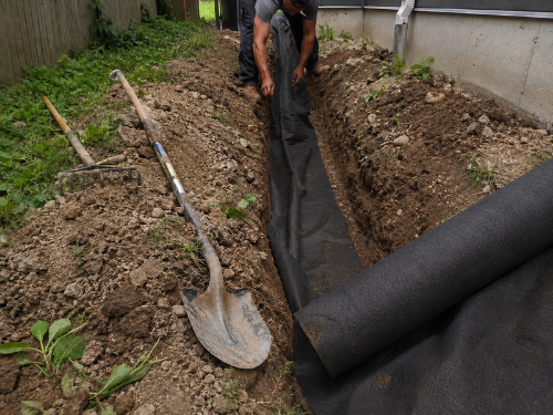 Installing non-woven geotextile drainage fabric in a trench along a foundation
