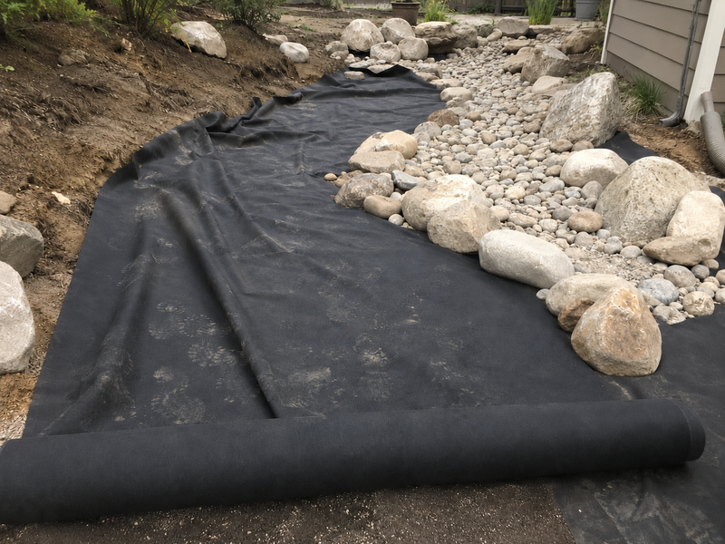 Non-woven geotextile fabric underlayment beneath a backyard dry creek bed
