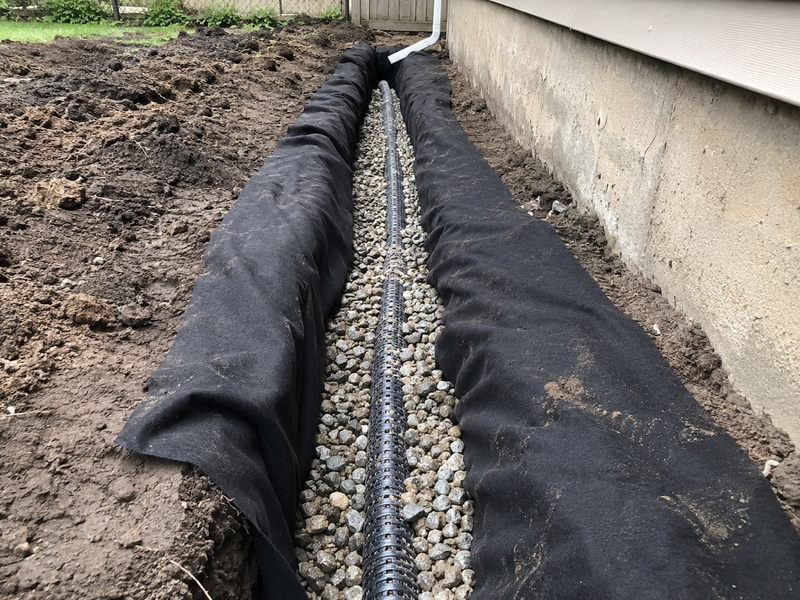 Non-woven geotextile fabric wrapping a foundation French drain with perforated pipe and gravel
