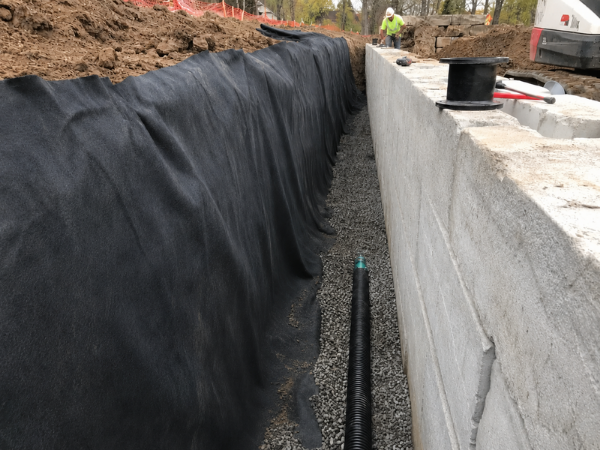 Non-woven geotextile filter fabric behind a retaining wall with gravel and drainage pipe
