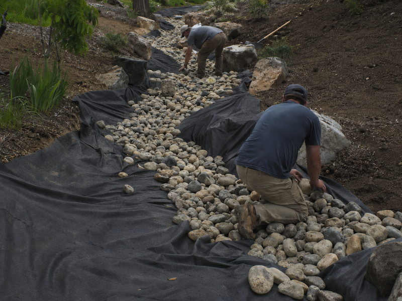 Workers placing river rock over non-woven geotextile fabric in a drainage swale

