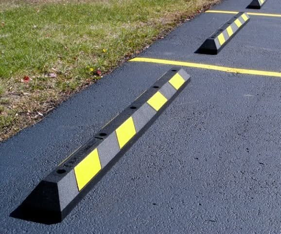 Black rubber parking stop with yellow reflective stripes installed at the edge of a paved driveway
