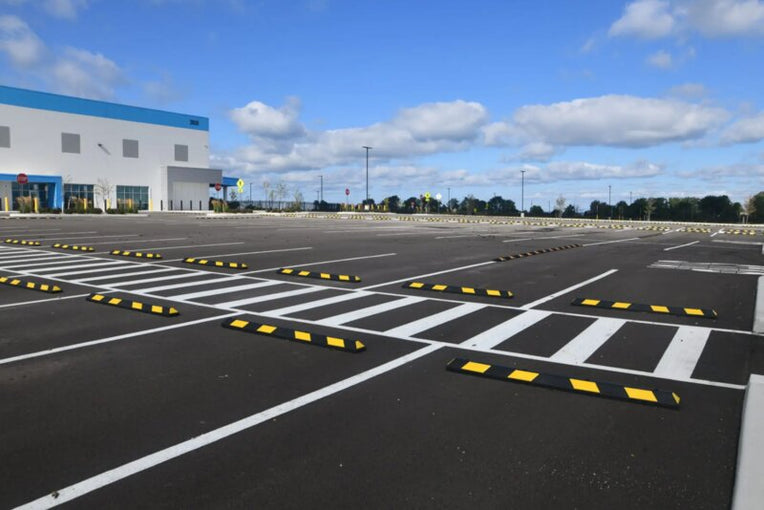 Rows of black and yellow rubber parking stops installed across a large commercial parking lot
