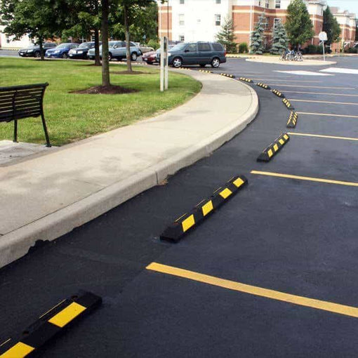 Black and yellow rubber wheel stops lining a curved parking lot at an apartment complex
