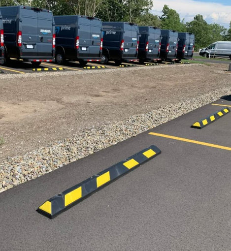 Black and yellow rubber wheel stops installed in a commercial parking lot lined with Amazon delivery vans
