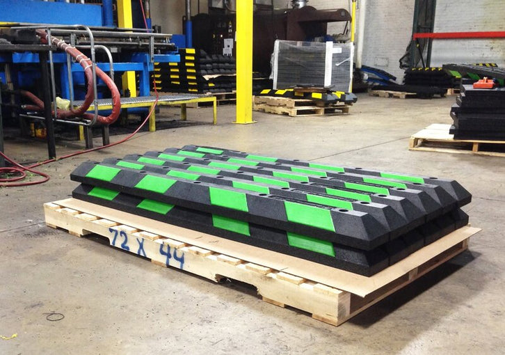 Stack of black and green rubber wheel stops on a pallet at the RubberForm manufacturing facility
