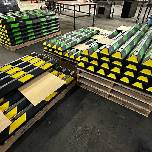 Pallets of black rubber parking stops with yellow and green reflective stripes ready for shipment
