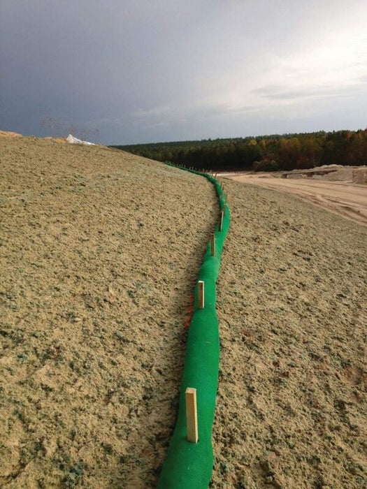 Silt sock installed as slope interruption on a sandy embankment under a stormy sky
